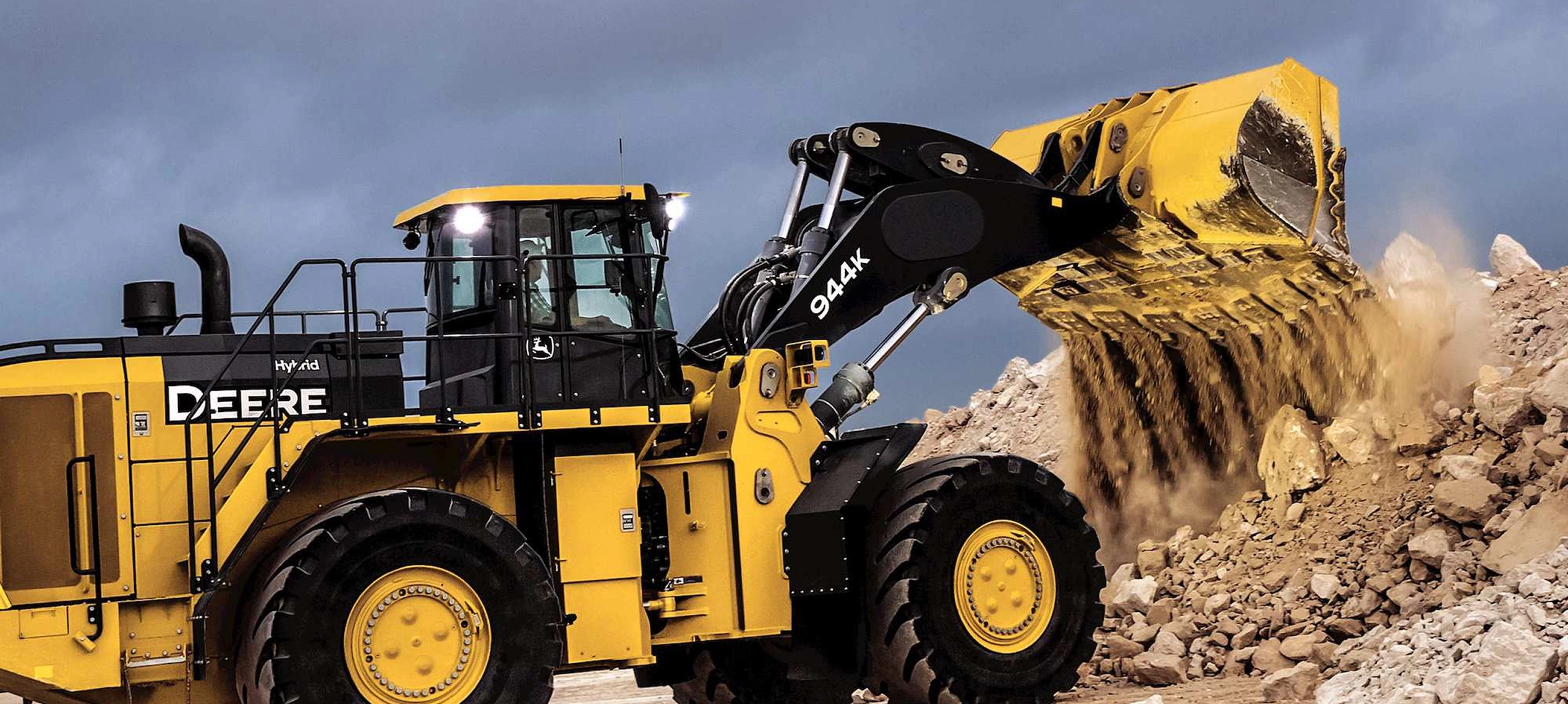 A John Deere loader empties its shovel onto a pile of concrete. 